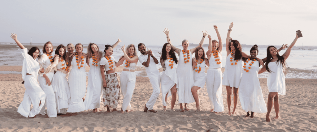 Group of yoga teacher training students celebrating in white outfits on the beach in Bali