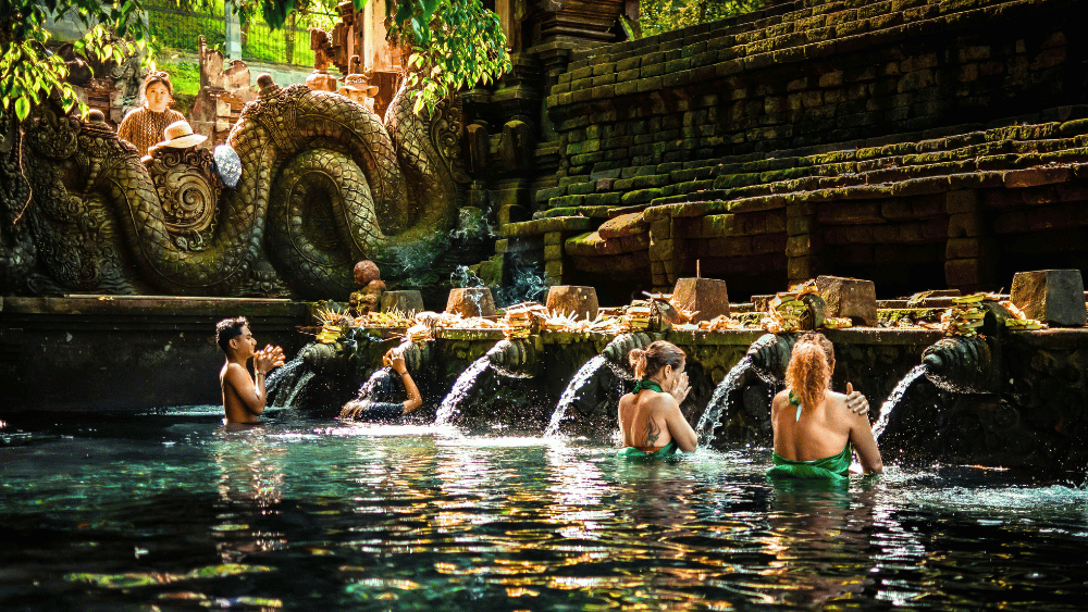 Why a Bali Yoga Retreat is Best in Sanur 2 Visitors participating in a traditional water purification ritual at Pura Tirta Empul, a sacred Hindu temple in Bali known for its holy spring water.